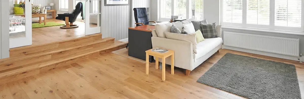 A modern living room with professionally installed laminate flooring, a beige sofa, a small side table, a gray rug, and large windows with white shutters in Bloomington, IN